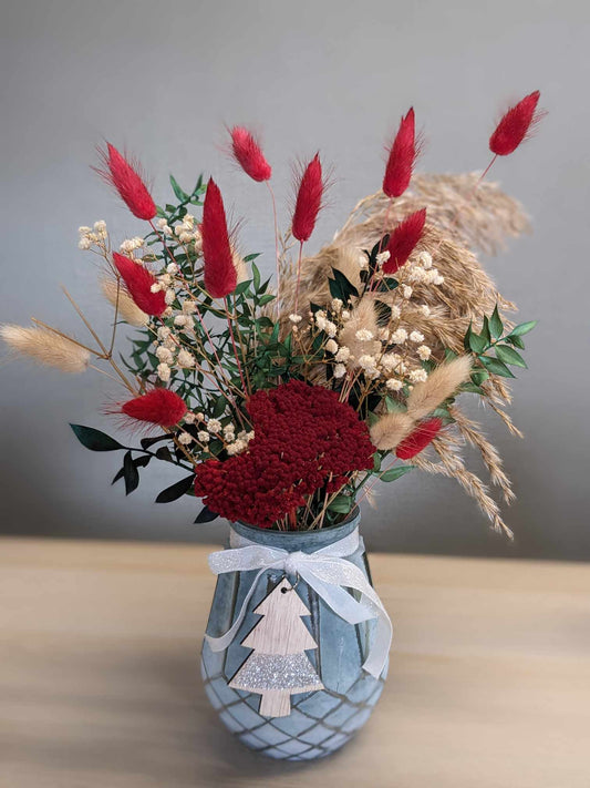 A blue snowy glass vase filled with a vibrant bouquet of colorful flowers rests on a wooden table.